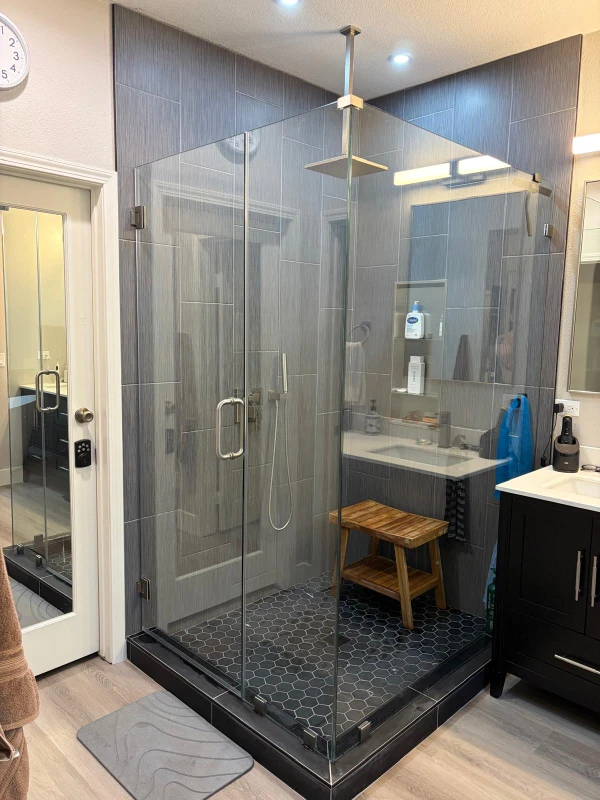 Custom walk-in glass shower with black hexagon floor tiles and gray wall tiles by Nikolic Construction